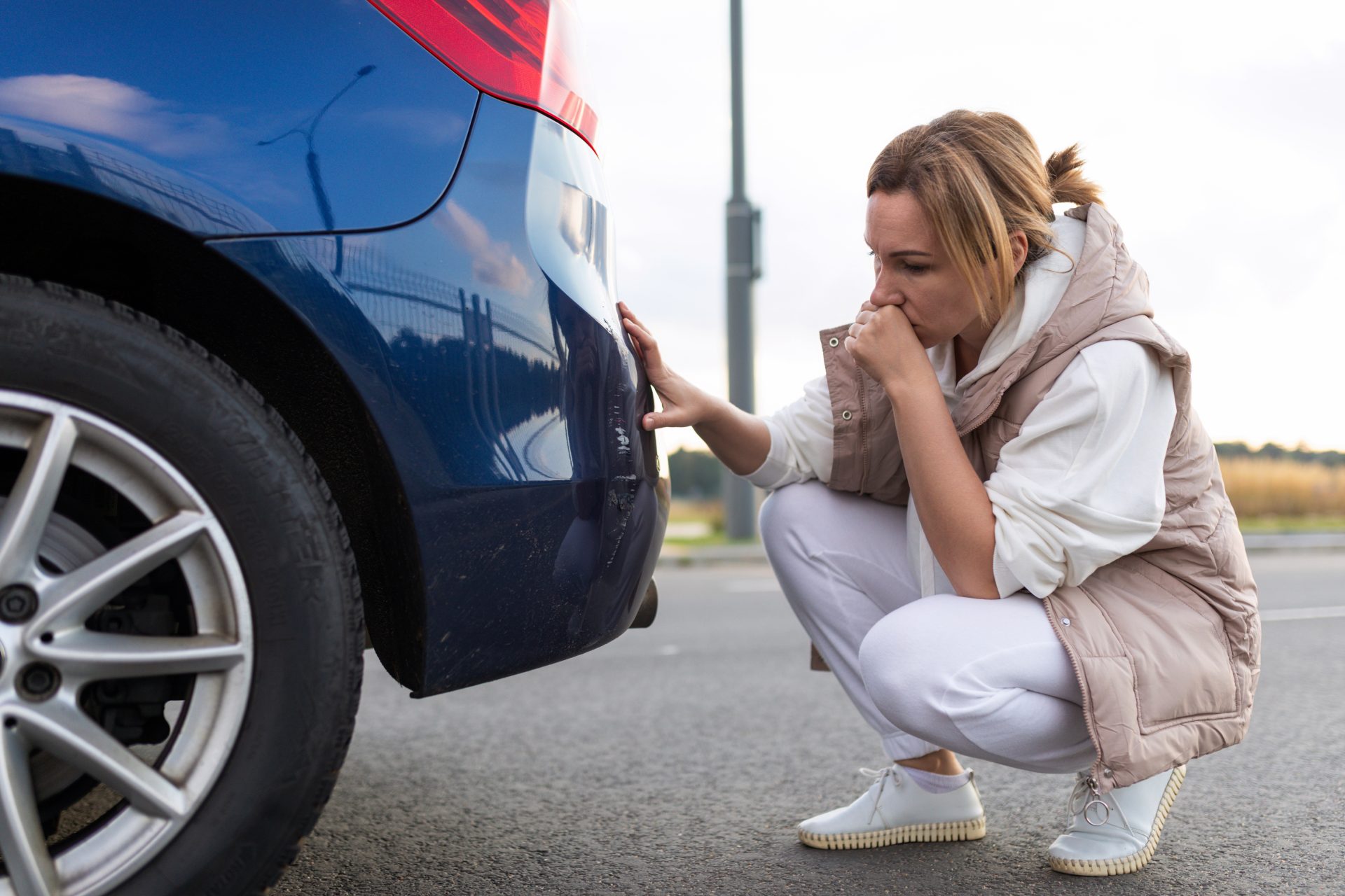 A woman squatting down to inspect the tire of her car.