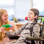 A handicapped boy sitting on a chair playing with a girl